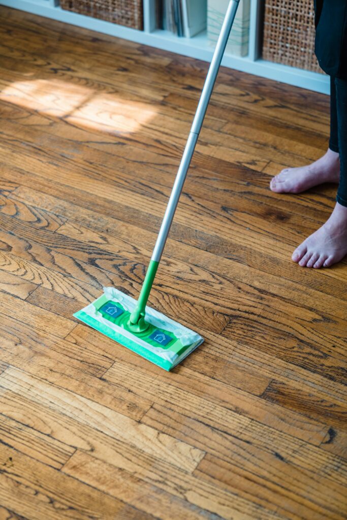 Person sweeping a wooden parquet floor with a green mop, indoors.